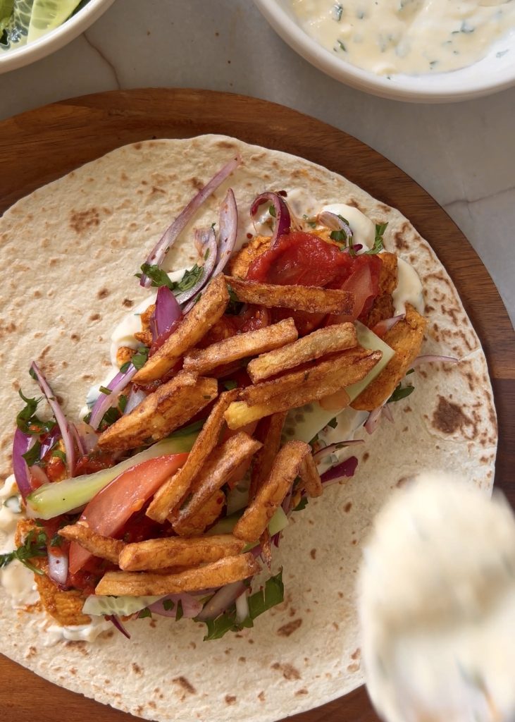Assemble the Wraps
Spread garlic sauce and harissa on each wrap. Add chicken, sumac onions, cucumber, tomato, and fries. Roll tightly and serve warm.