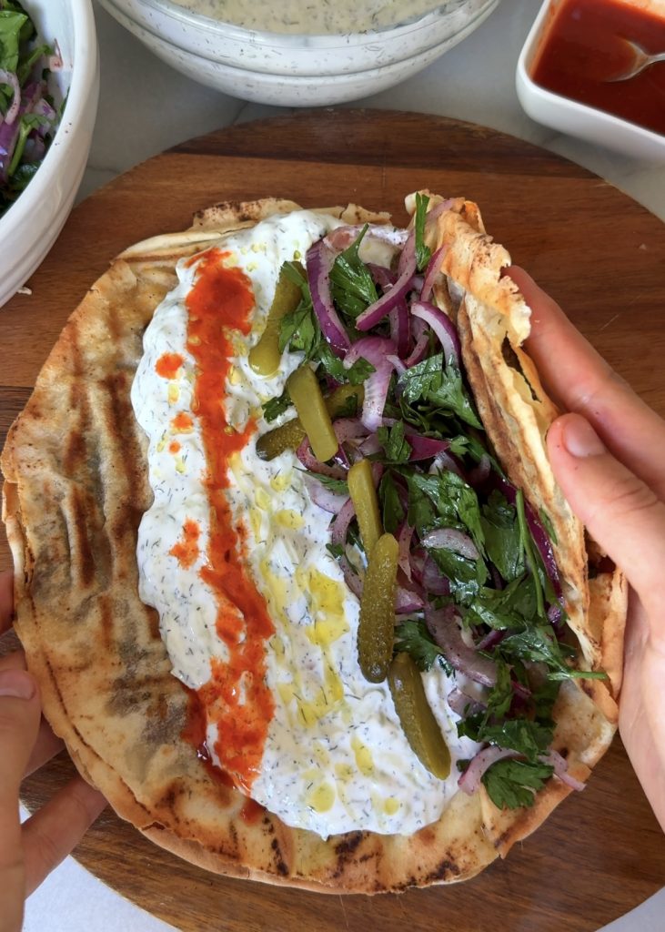 Prepare the Sauces and Salad:
Mix Greek yogurt, grated cucumber, dill, lemon juice, garlic powder, and salt for the white sauce. In another bowl, whisk harissa, sriracha, and a little water for the spicy sauce. Toss sliced red onion with sumac and parsley for the salad.