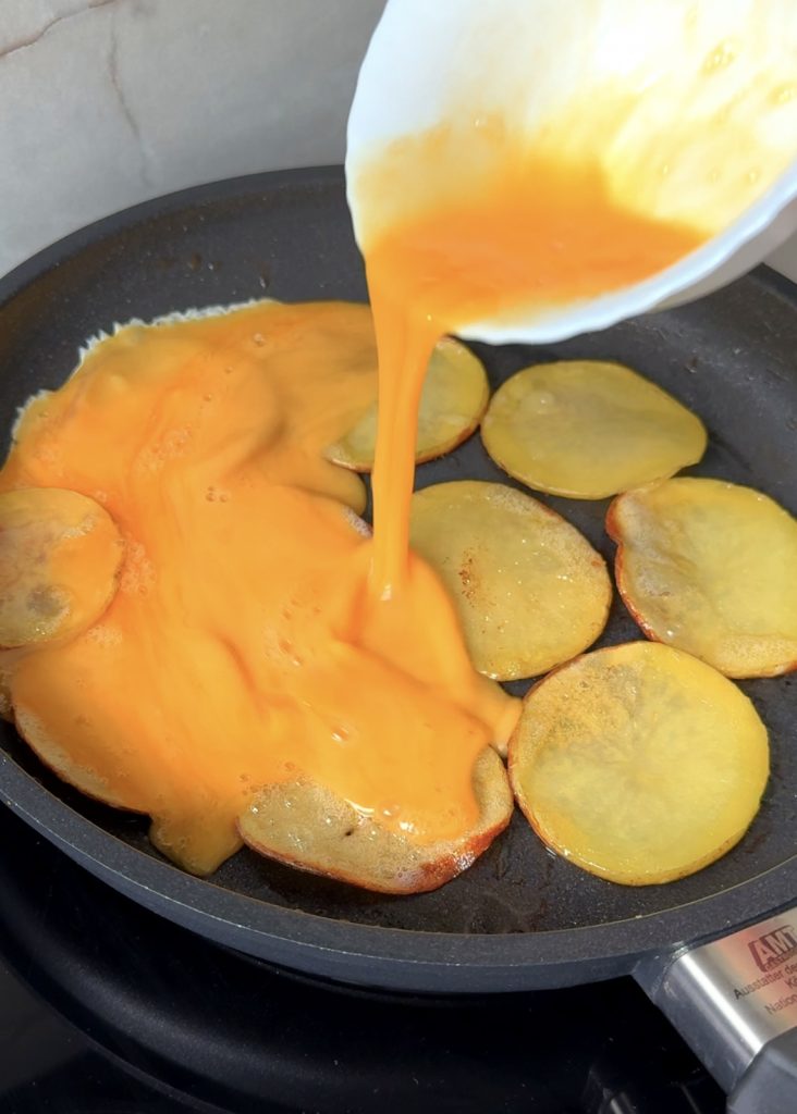 Cook the Potato Base
Melt butter and olive oil in a non-stick pan. Thinly slice the potato and arrange the slices in a circular pattern, slightly overlapping to form the base. Cover and let them soften and turn golden.