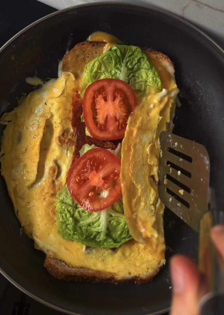 Add veggies + fold. Add greens and tomatoes, fold the eggs inward, and close the toast into a warm sandwich. 