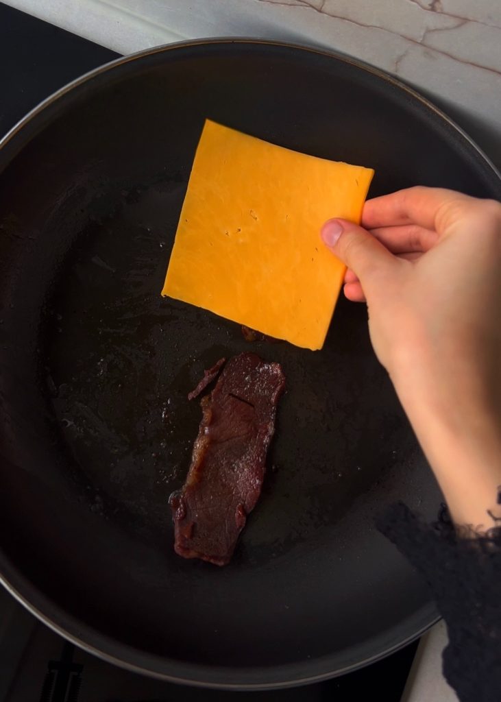 Crisp the pastırma, then add the cheese and eggs. Let the pastırma turn lightly golden, melt the cheddar over it, and pour in the beaten eggs.