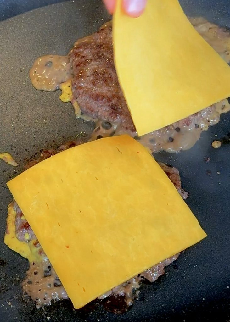 Cook the patties in a hot pan, spread mustard on one side, flip, and top with cheddar. Use two patties per burger.