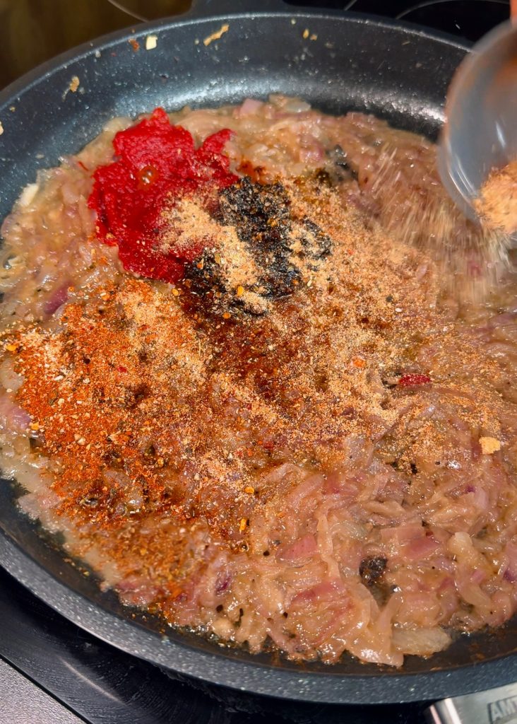 Caramelize the onions in butter and olive oil, then stir in garlic, tomato paste, chili oil, pasta water, and spices until fragrant.