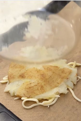 Pressing a boiled potato half flat over shredded mozzarella