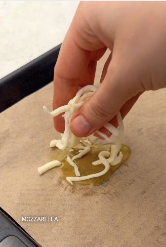 Adding shredded mozzarella to olive oil on a lined baking tray