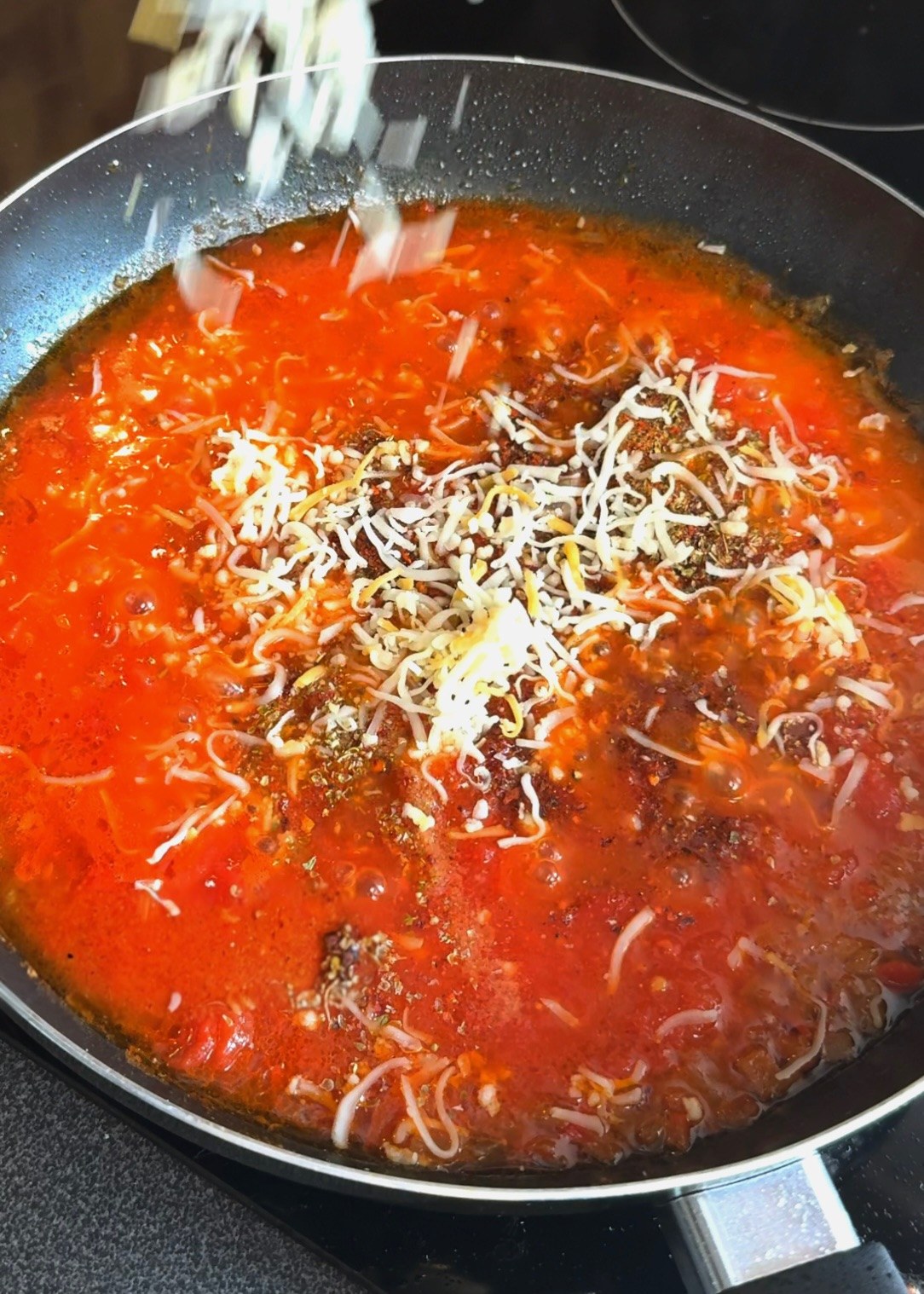 Adding shredded mozzarella to the spiced tomato sauce