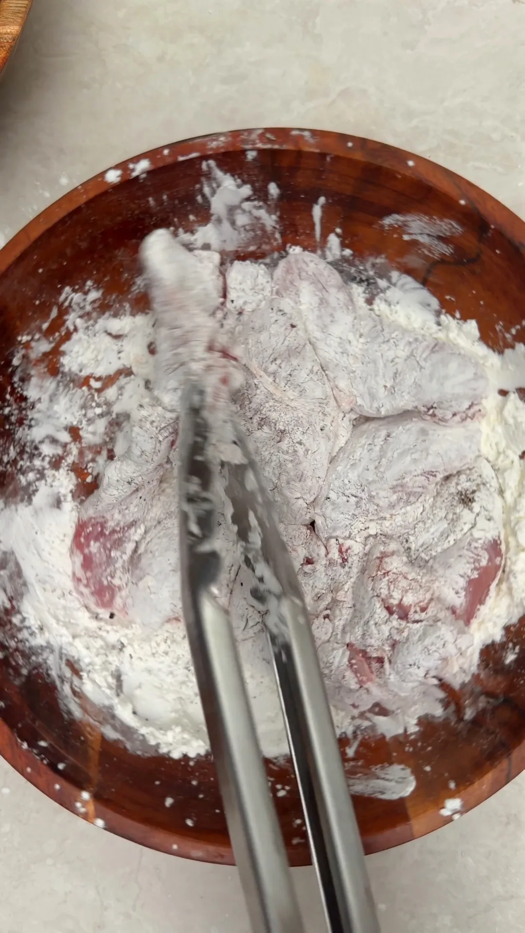 Chicken thighs coated in cornstarch in a wooden bowl