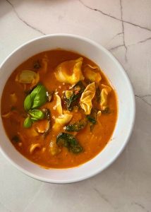Creamy tomato tortellini soup with spinach in a white bowl