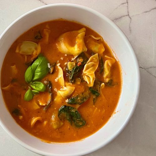 Creamy tomato tortellini soup with spinach in a white bowl