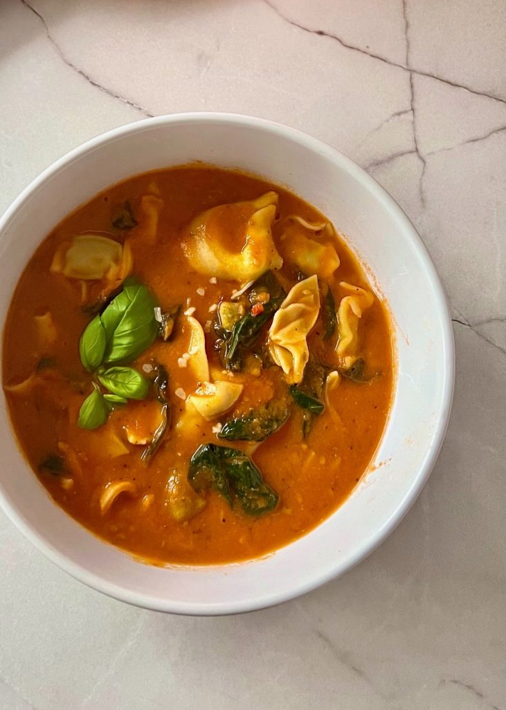 Creamy tomato tortellini soup with spinach in a white bowl